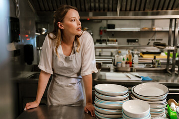Young blonde woman holding plates while working in restaurant kitchen