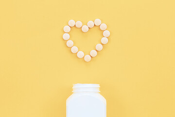 Scattered heart shaped pills on yellow background, flat lay.