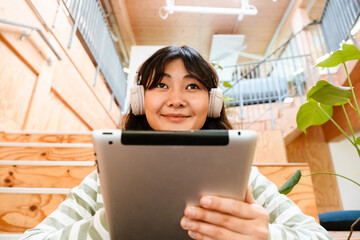 Asian woman using tablet computer and headphones while sitting indoors