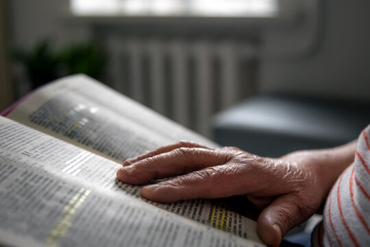 An old woman reads the Bible, hands close up.