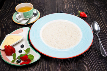 breakfast milk porridge on a dark background with berries in a saucer

