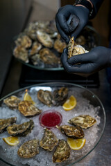 chef opens an oyster over a plate of oysters in a dish on ice
