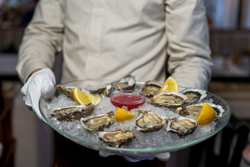 open oysters in a large dish on ice in the hands of a waiter
