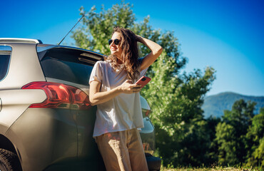 Happy young woman driver traveler in sunglasses using smartphone during summe adventure travel