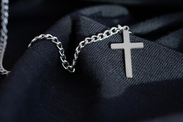 silver or stainless steel necklace with a cross pendant rests on a black cloth