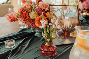 Detail of a table setting in a restaurant. Fresh flowers in a small vase on a green tablecloth. Next to the flowers is a candle in a glass candlestick.
