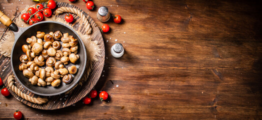 Frying pan with fried mushrooms on a wooden tray. 