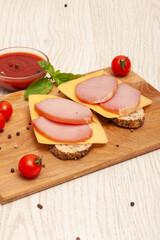 Sandwiches with ham and cheese on a wooden board decorated with cherry tomatoes and basil