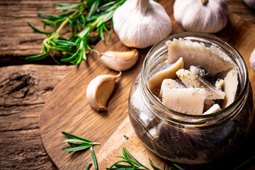 Pieces of salted herring in a glass jar on a cutting board.