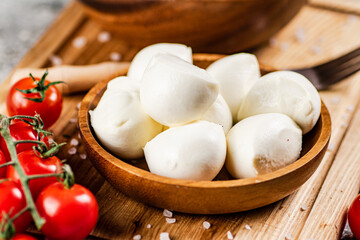 Mozzarella cheese on a wooden cutting board with cherry tomatoes. 