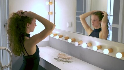 Young ballerina fixing her hair into a pony tail in front of the mirror.