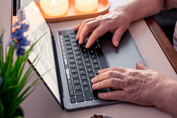 Retired woman uses laptop, hands close up.
