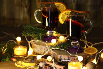 mug of mulled wine with decoration and candles on dark wooden background