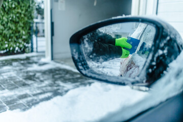 Fototapeta na wymiar Teenager cleans car after a snowfall, removing snow and scraping ice