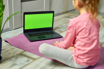Little girl watching online video on laptop and doing stretching, fitness exercises at home