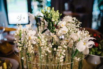 Wedding decor on the festive table for the party. The composition of white lilies of the valley and greenery for the wedding table. Close up.