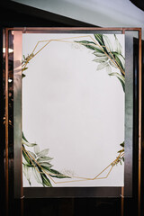 Seating table. Tables wedding guests on easel on wedding reception. The frame is decorated with green flowers and greenery. List, plan, chart of the seating area of guests at tables at restaurant.