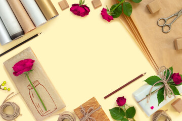 Gifts in paper wrapping, set of vintage yellow package paper, rolls, ropes and pencils for decoration. Bouquet of red roses on yellow vintage background