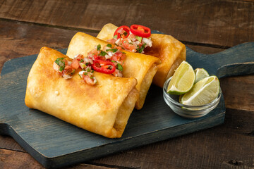Mexican traditional chimichanga close-up made from corn flour tortillas stuffed with minced meat and beans with various spices. Wooden background
