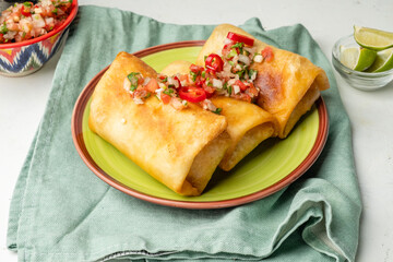 Chimichinga, burritos in a plate poured with salsa sauce with tomatoes, light background.