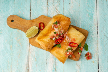 Chimichanga or Mexican-style burrito on a wooden board in tomato salsa sauce, top view.