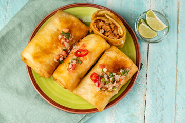 Chimichanga three pieces in a green plate, top view. Traditional Mexican cuisine.