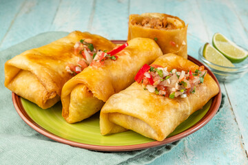 Delicious chimichanga or tortilla burrito stuffed with minced meat, spices and beans in a green plate, blue wooden background, close-up.