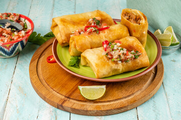 Chimichanga or burrito on a green plate with salsa sauce. Mexican traditional snack.