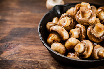 A frying pan with fried mushrooms on the table. 