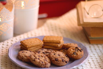 Plate of cookies, cup of tea, fresh blueberries, dry oranges, stack of books, reading glasses and tablet on the table. Hygge at home. Selective focus.