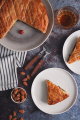 Top view of traditional French galette des rois cake cut in pieces in a white plates with almonds and forks. A traditional cake usually served on Epiphany, made with puff pastry and creamy almond fill