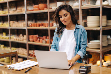 Young ceramic shop owner using a laptop in her store