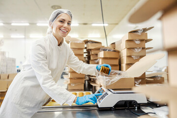 A happy food factory worker is measuring cookies on scales and putting them in a box.