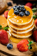 A pile of pancakes with fresh berries and honey on the table. 