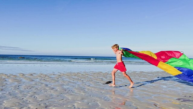 Child with colorful parachute flying on wind run at ocean beach