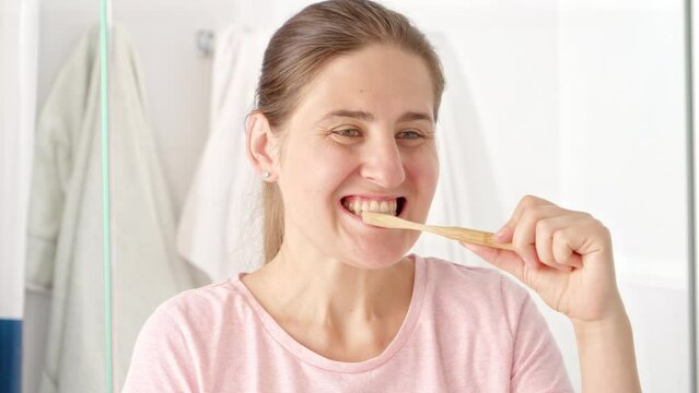 Beautiful young woman brushing her teeth at the mirror in bathroom. Concept of teeth health, self checking mouth and oral hygiene