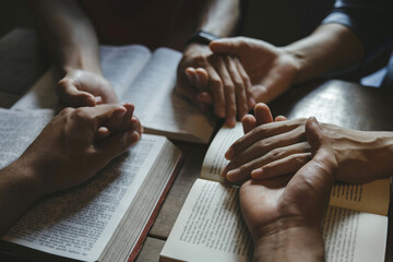 Group of people holding hands praying worship believe with bible on a wooden table for devotional...