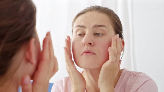 Closeup portrait of beautiful young woman checking for new wrinkles and pimples on her face skin. Concept of female aging, skin issues, facial treatment and care