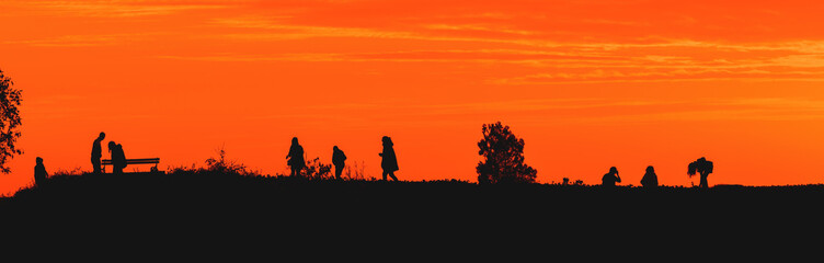 Obraz na płótnie Canvas Silhouette of young people in sunset with beautiful orange sky in background, youth lifestyle and fun concept