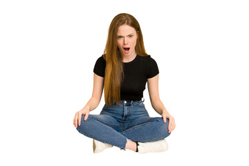 Young redhead woman sitting on the floor cut out isolated shouting very angry, rage concept, frustrated.