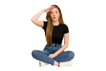 Young redhead woman sitting on the floor cut out isolated shouts loud, keeps eyes opened and hands tense.