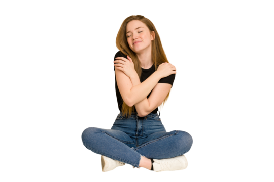 Young redhead woman sitting on the floor cut out isolated hugs, smiling carefree and happy.