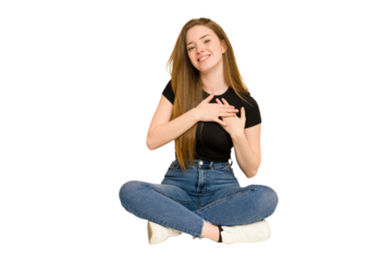 Young redhead woman sitting on the floor cut out isolated has friendly expression, pressing palm to chest. Love concept.