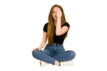 Young redhead woman sitting on the floor cut out isolated having fun covering half of face with palm.