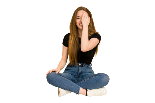 Young redhead woman sitting on the floor cut out isolated having fun covering half of face with palm. - Powered by Adobe