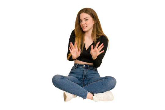 Young redhead woman sitting on the floor cut out isolated laughing about something, covering mouth with hands. - Powered by Adobe