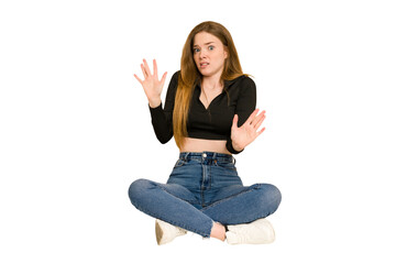 Obraz premium Young redhead woman sitting on the floor cut out isolated indicates with both fore fingers up showing a blank space.