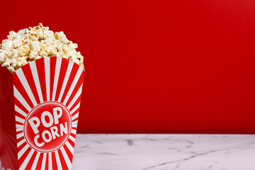 Salted popcorn in carton package on white marble and red background. Copy space	