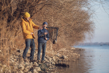 Father and son are fishing on sunny winter day. They caught a fish and are holding it in a landing net.