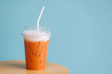 ice thai milk tea in plastic cup with white straw on woonden table and blue vintage wall.  thai...